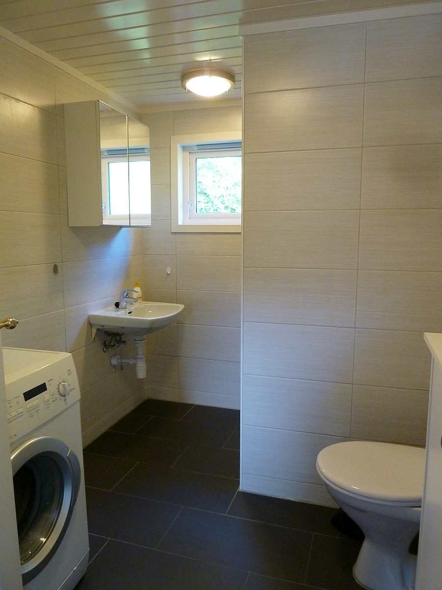 Das Badezimmer des Ferienhauses mit WC, Dusche, Waschbecken und Waschmaschine. Fußbodenheizung vorhanden.