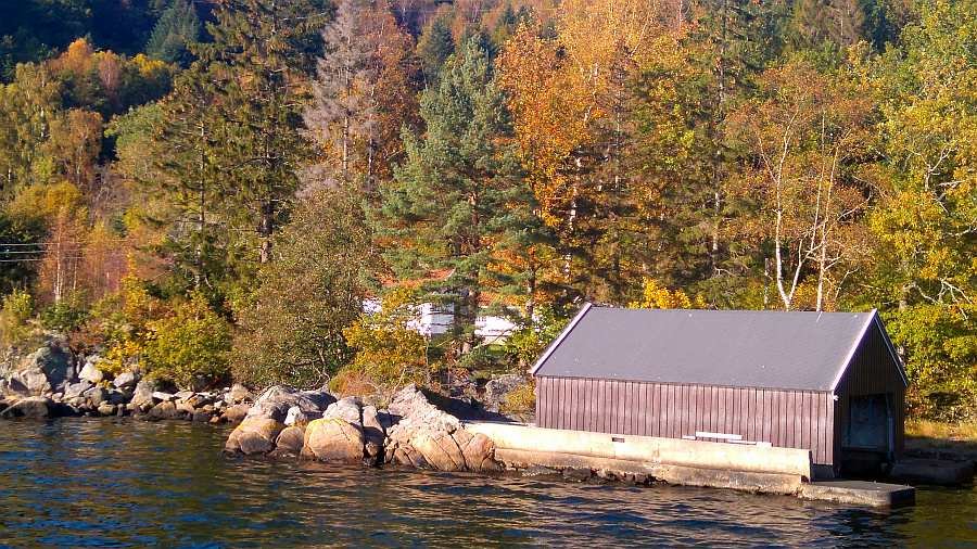 Blick vom Wasser auf das Bootshaus und das Grundtstück - im Hintergrund kann man das Wohnhaus erkennen